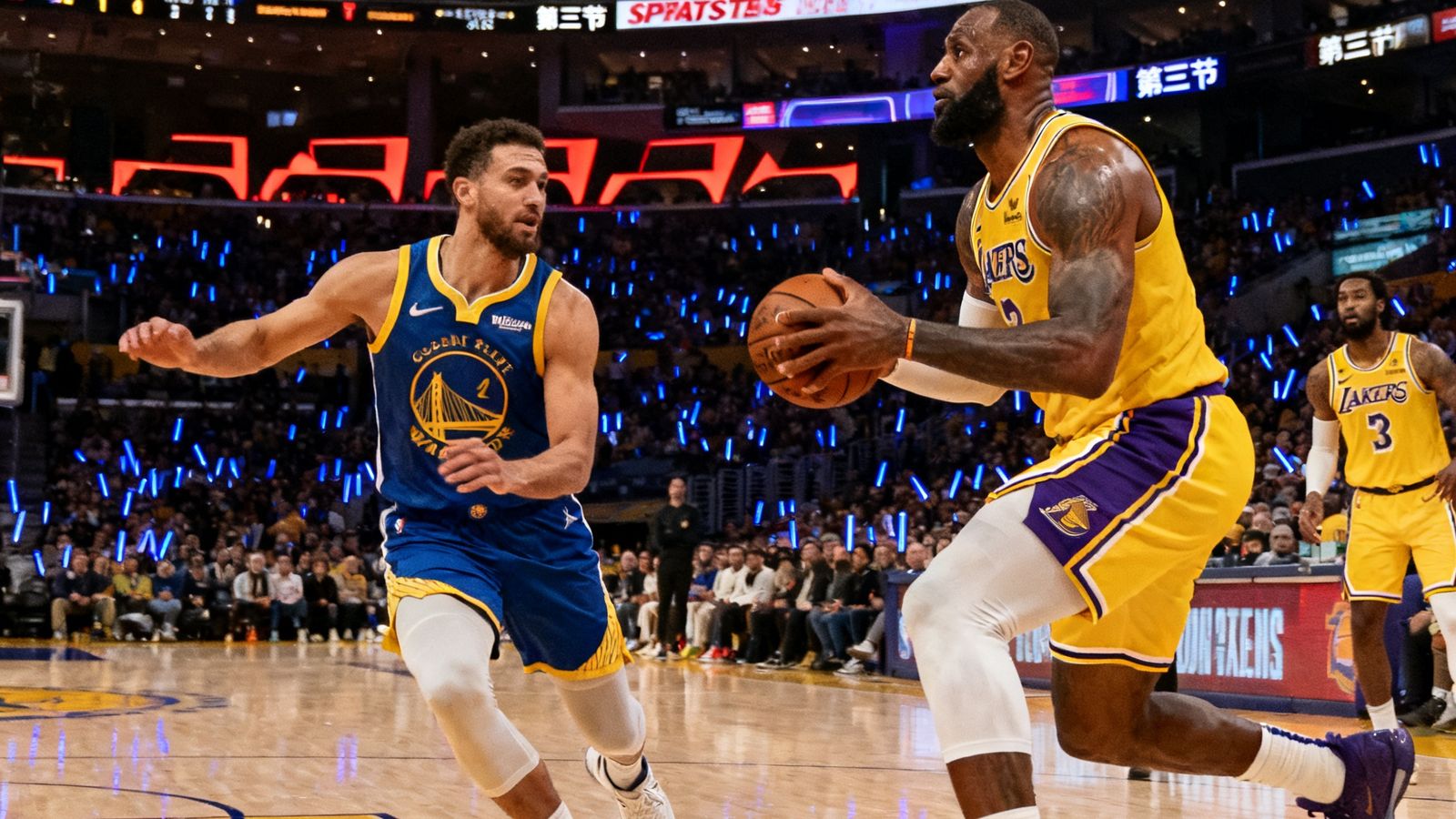NBA常规赛洛杉矶湖人主场对阵金州勇士的比赛画面，斯台普斯中心灯光璀璨，詹姆斯持球突破瞬间被捕捉，比分牌显示第三节